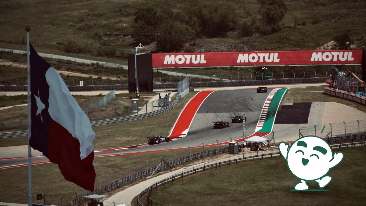 Cars climb the hill to Turn 1 at the Circuit of the Americas, with a Texas flag in the foreground.